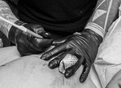 Foto en blanco y negro de las manos de un tatuador con guantes, tatuando en Kaifa´s tattoo studio en madrid, zona de MONCLOA