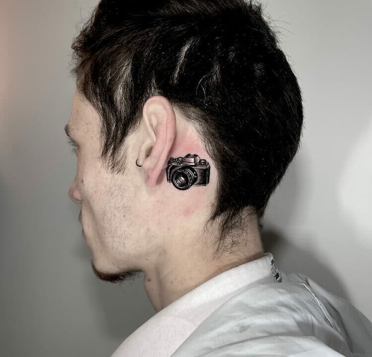 Foto de un tatuaje de una cámara de fotos detrás de la oreja tatuado en kaifa´s tattoo Studio Madrid, con materiales cruelty free, tattoo de cara femenina mujer