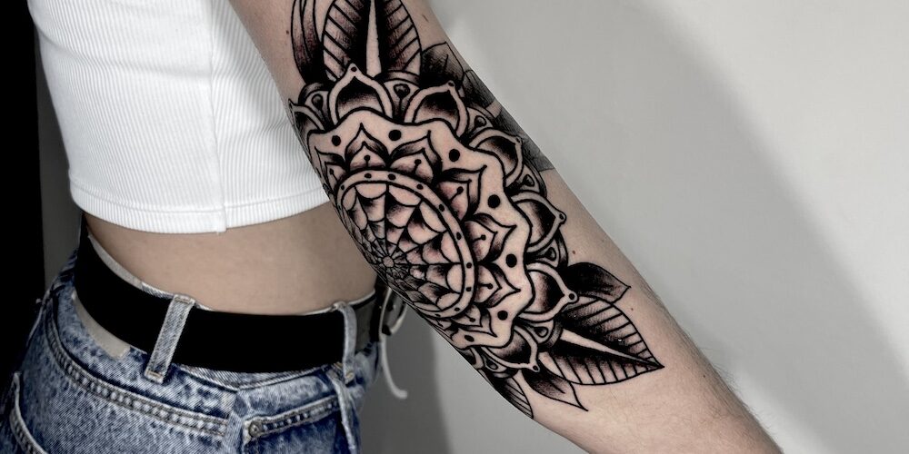 Foto de una mujer joven con el brazo tatuado en la zona del codo con estilo blackwork en un tatuaje ornamental por Carlos cuervo, tatuador de kaifa´s tattoo studio en Madrid