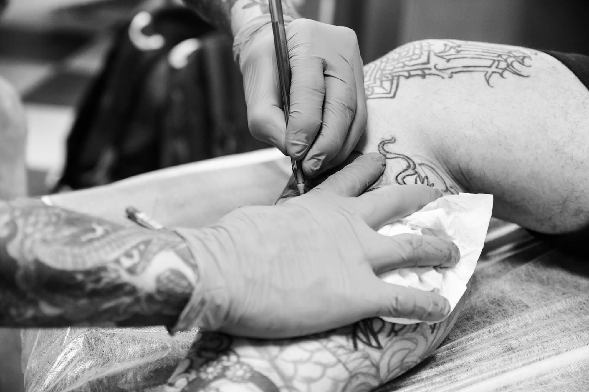 foto en blanco y negro en el Estudio de tatuajes y piercings Kaifa´s Tattoo Madrid en la zona de Chamberí. Se ven las manos de un tatuador haciendo un tattoo a un cliente con tinta vegana
