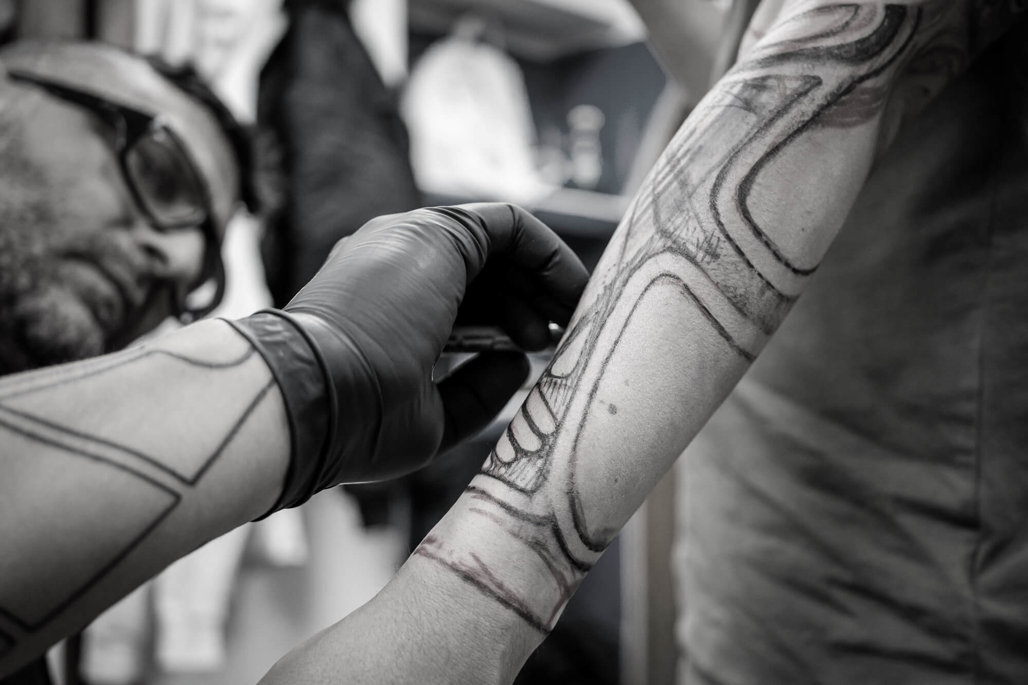 foto en blanco y negro en el Estudio de tatuajes y piercings Kaifa´s Tattoo Madrid en la zona de Chamberí. Se ve a un tatuador tatuando el brazo de un cliente con tinta vegana