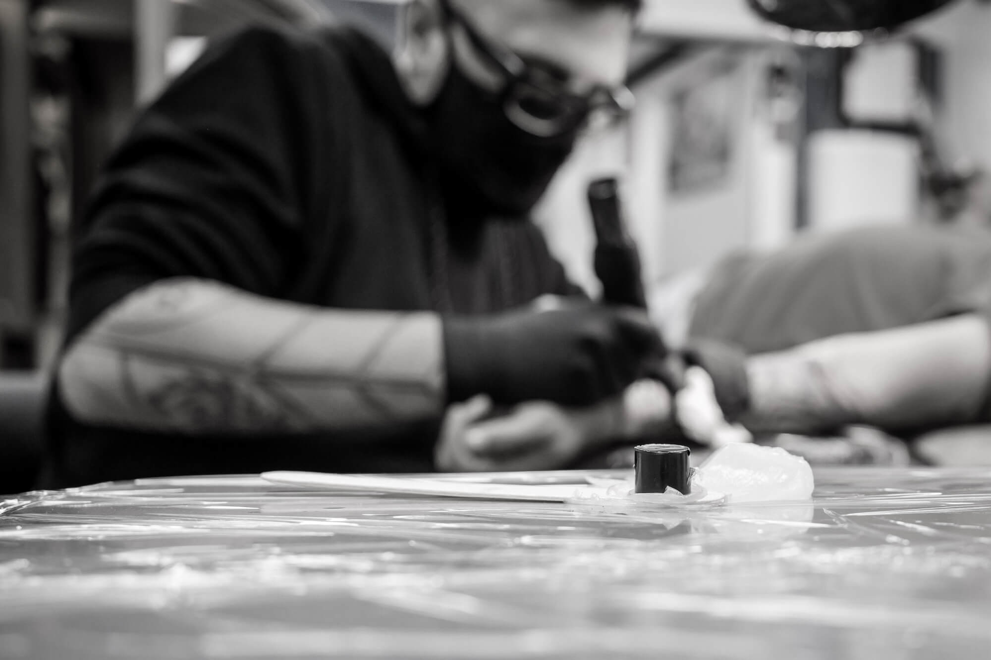 foto en blanco y negro en el Estudio de tatuajes y piercings Kaifa´s Tattoo Madrid en la zona de Chamberí. Se ve un tatuador con mascarilla