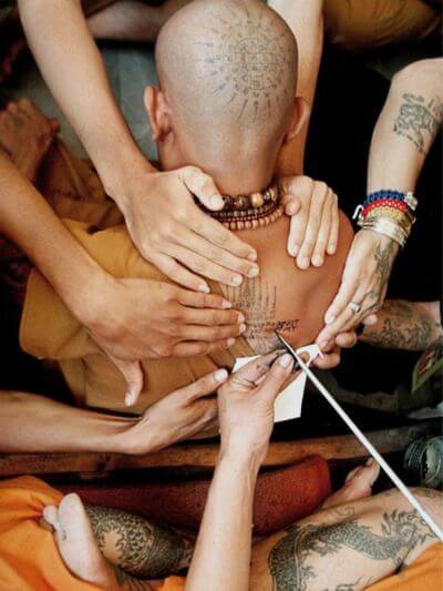 foto de un hombre semi recostado, con la espalda sostenida por las manos de varias personas, mientras le tatuán la espalda con estilo poked, como en el estudio de tatuajes y piercings kaifa en Madrid